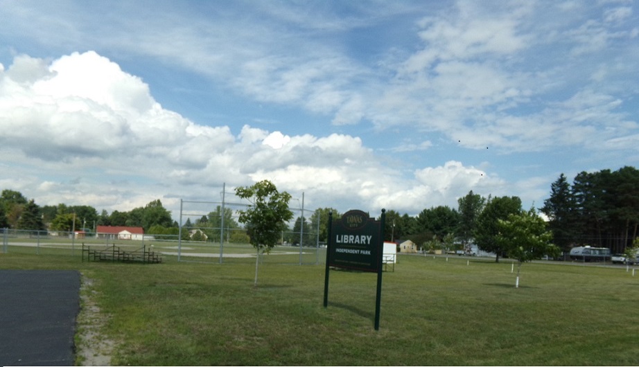 picture of Tawas City Library and Independent Park sign. Baseball field in background