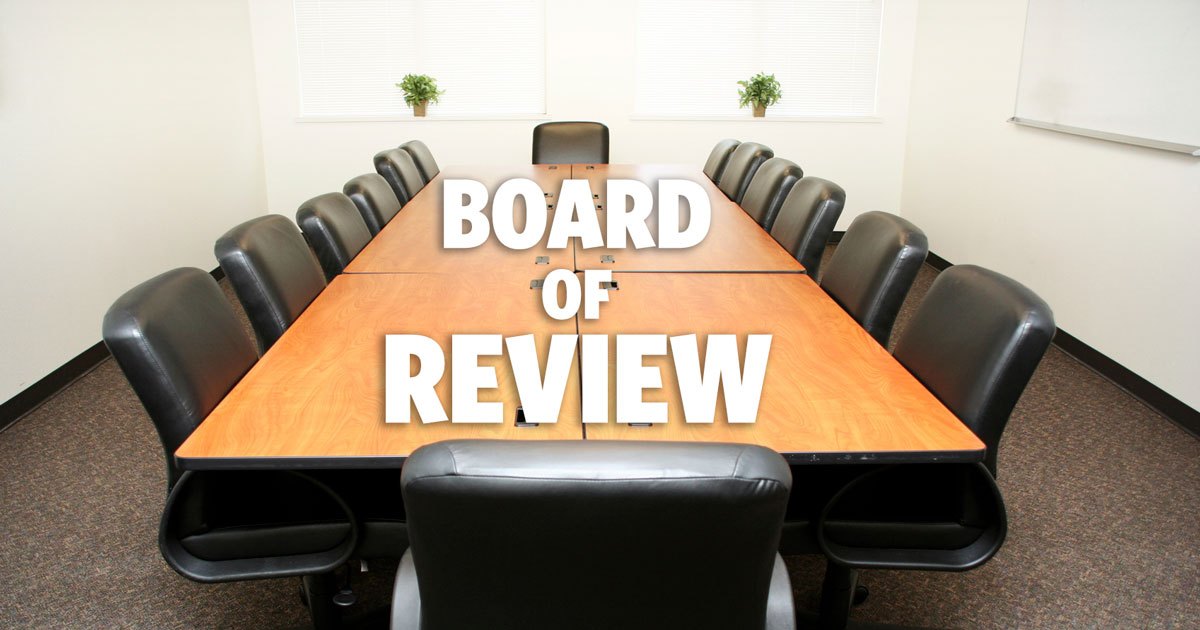 Long wood conference table with black leather chairs around the table with words on table that say Board of Review